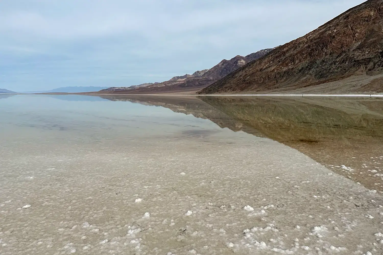 Blick vom mit Wasser gefüllten Badwater Basin zum Death Valley mit Spiegelung